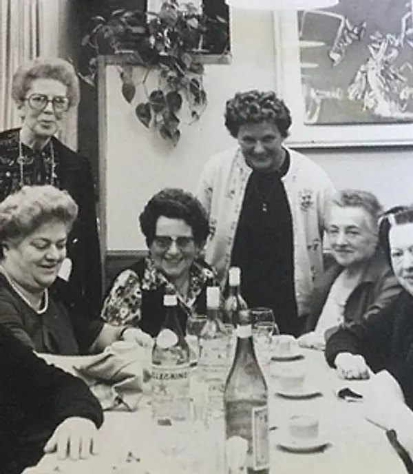 Una tavolata di signore in una foto in bianco e nero, con le bottiglie in tavola